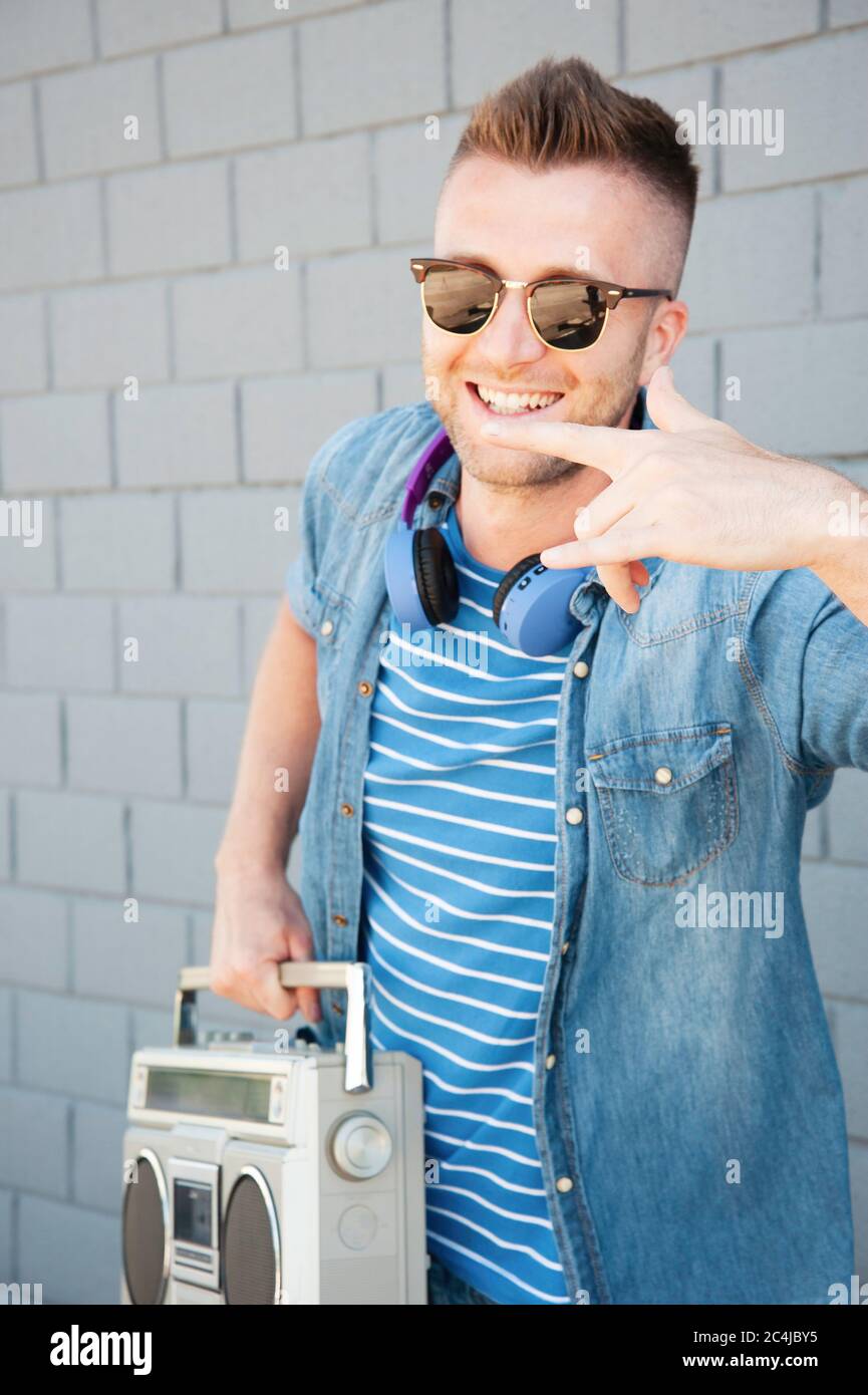 Young crazy man with 80's boombox stereo playing rock music with gray wall background - Trendy guy having fun dancing outdoors with vintage radio - Jo Stock Photo