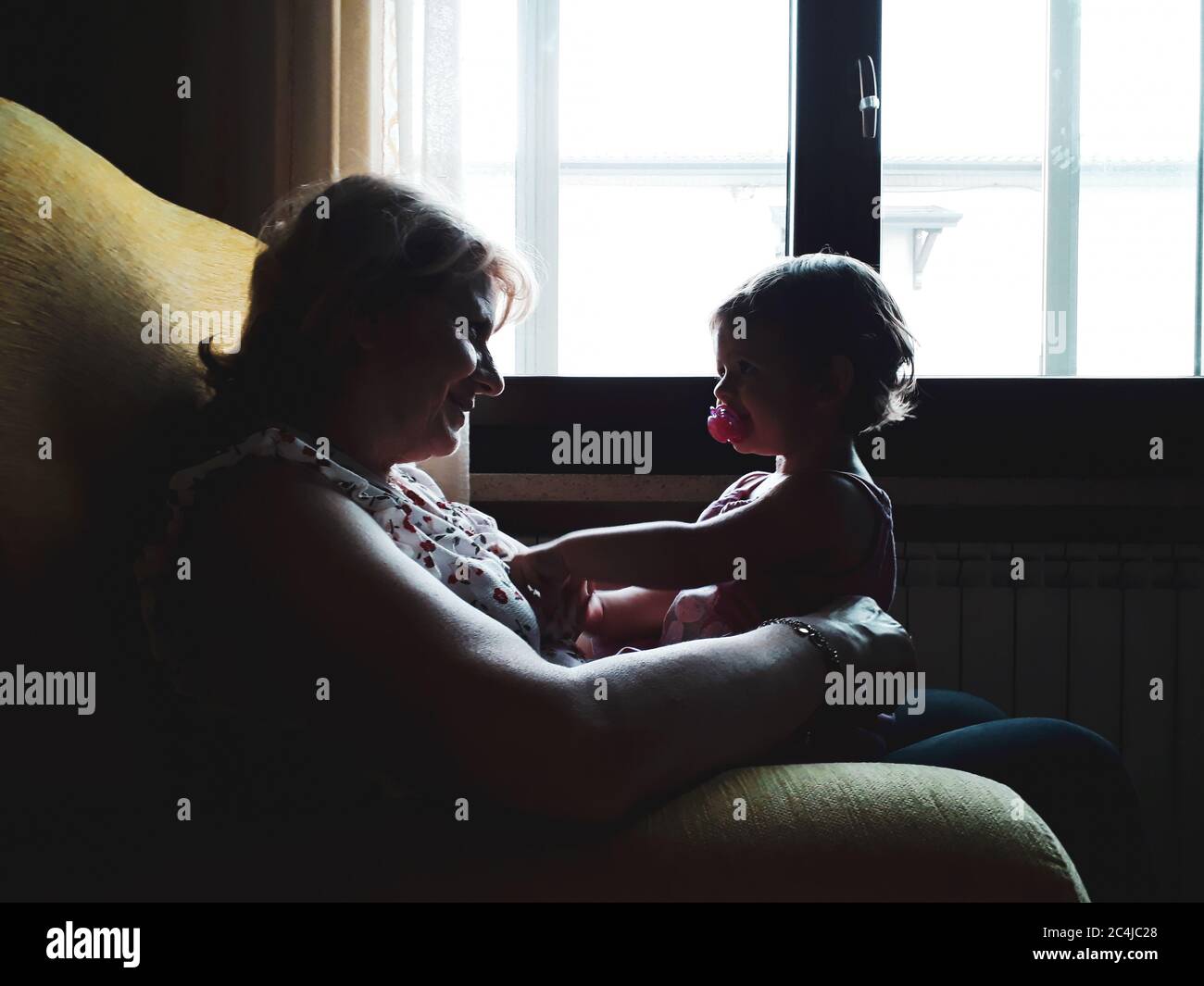 Little girl with pacifier sitting on grandmother's legs in the living room  at home - Happy middle-aged grandmother show love and affection - Granny pl  Stock Photo - Alamy