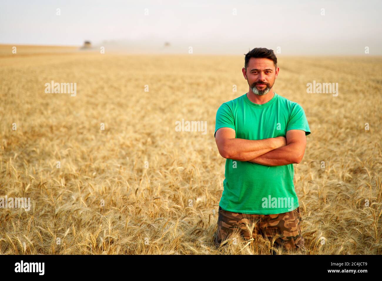Happy farmer proudly standing in wheat field with arms crossed on chest ...