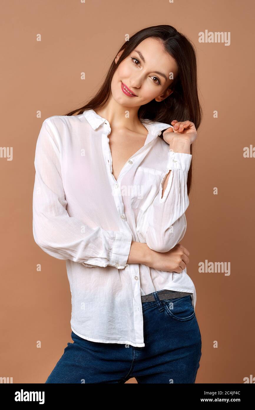 Beautiful girl in white shirt and blue jeans posing on brown background Stock Photo