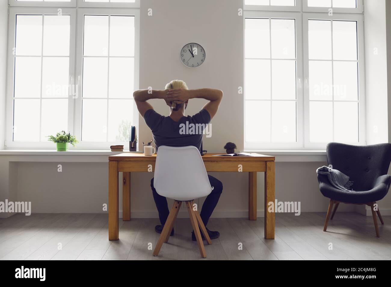 Back view. Man hands behind his head dreams of resting while sitting on