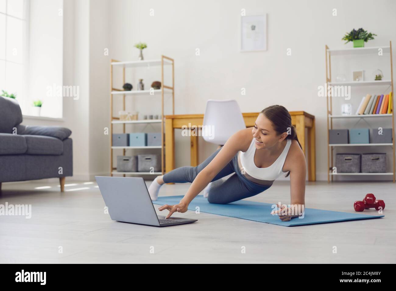 Online home fitness. Woman with laptop training to web video tutorial. Personal trainer giving yoga class via internet Stock Photo