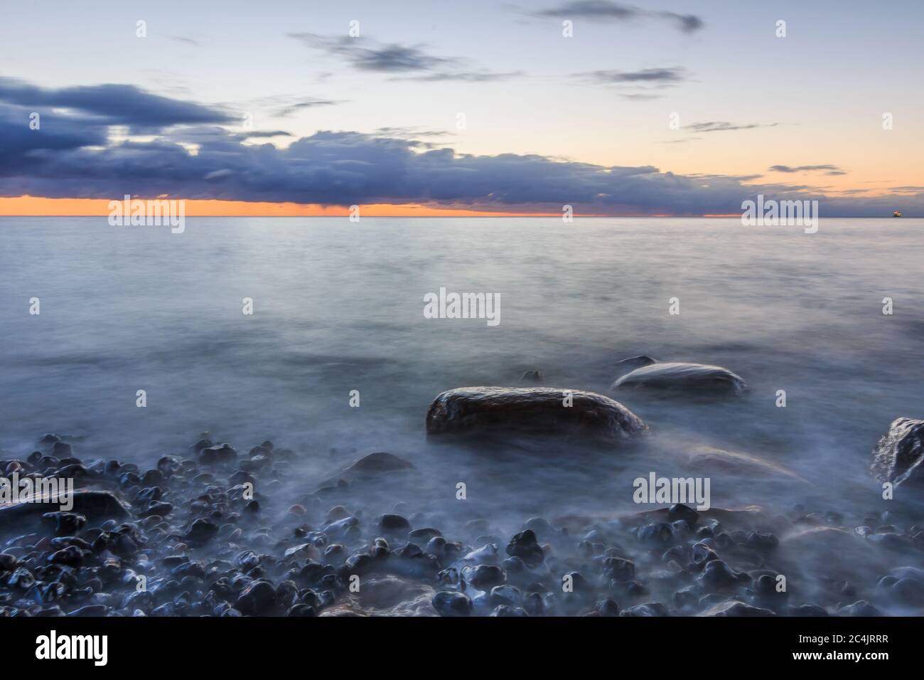 Baltic Sea on the island of Ruegen in the morning with sunrise. Dramatic clouds over the red colored horizon on the stony coastline. Large stones in t Stock Photo
