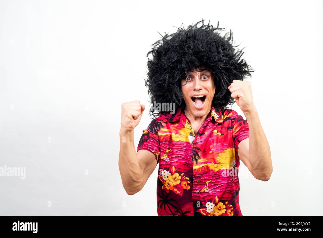 Man with afro wig and hawaiian shirt celebrating something, very happy. Mid shot. White background. Stock Photo