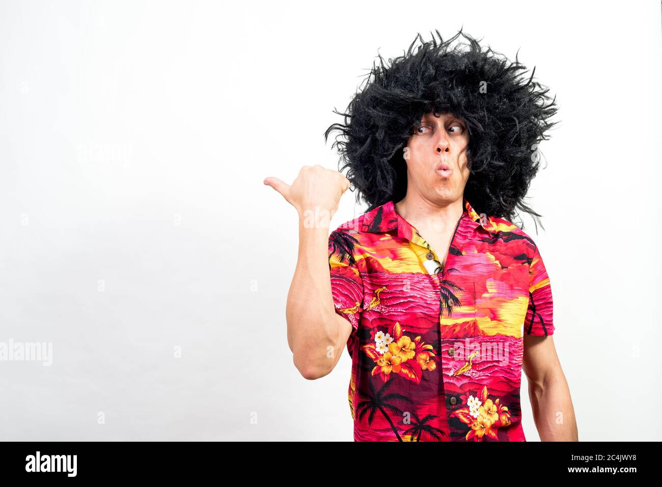 Man in afro wig and hawaiian shirt, pointing aside very surprised. Mid shot. White background. Stock Photo