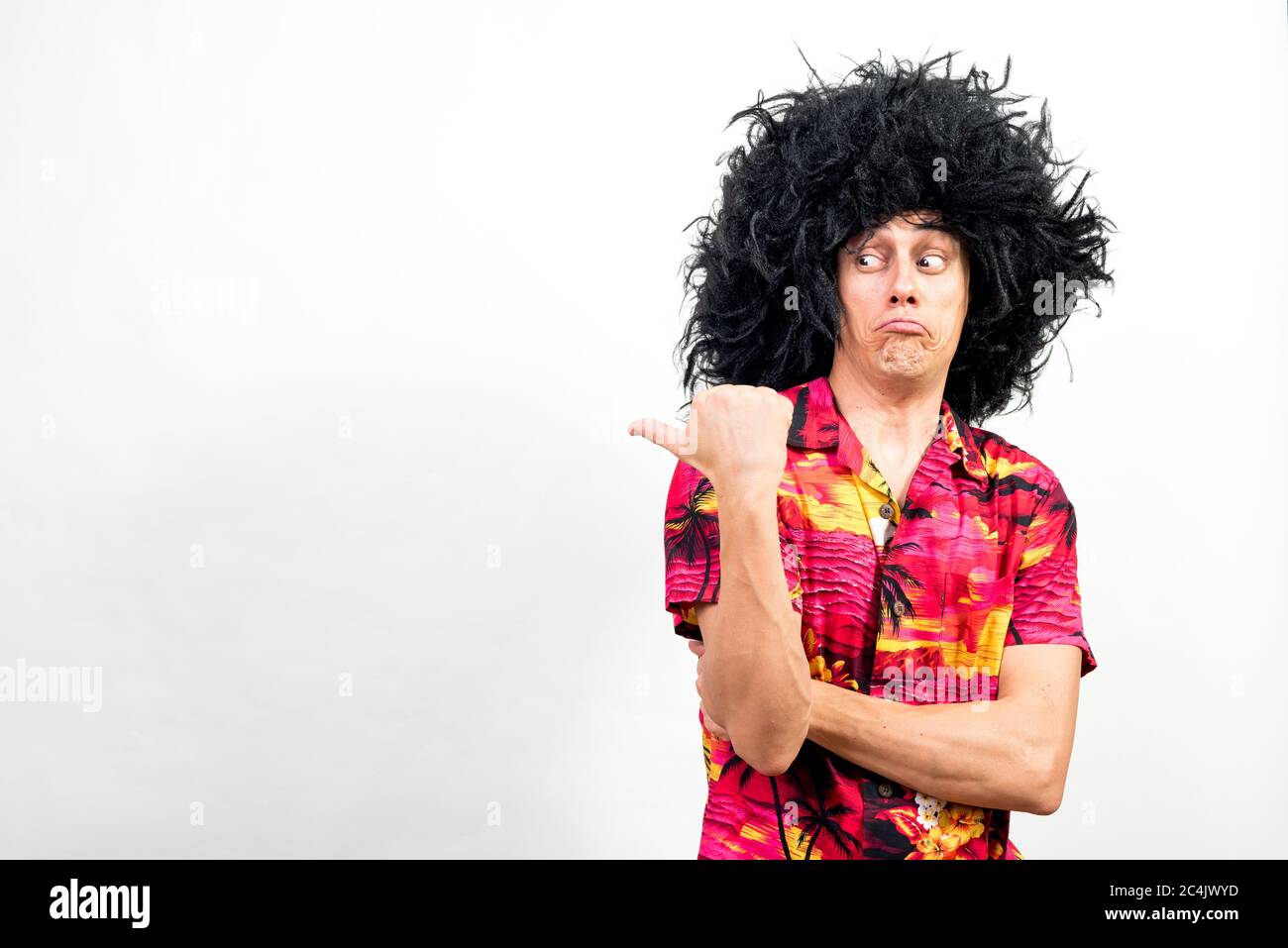 Man in afro wig and hawaiian shirt, pointing aside very surprised. Mid shot. White background. Stock Photo