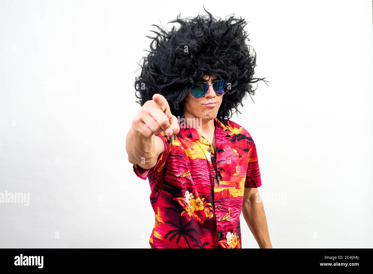 Man with afro wig, sunglasses and hawaiian shirt pointing ahead with boss attitude. Mid shot. White background. Stock Photo