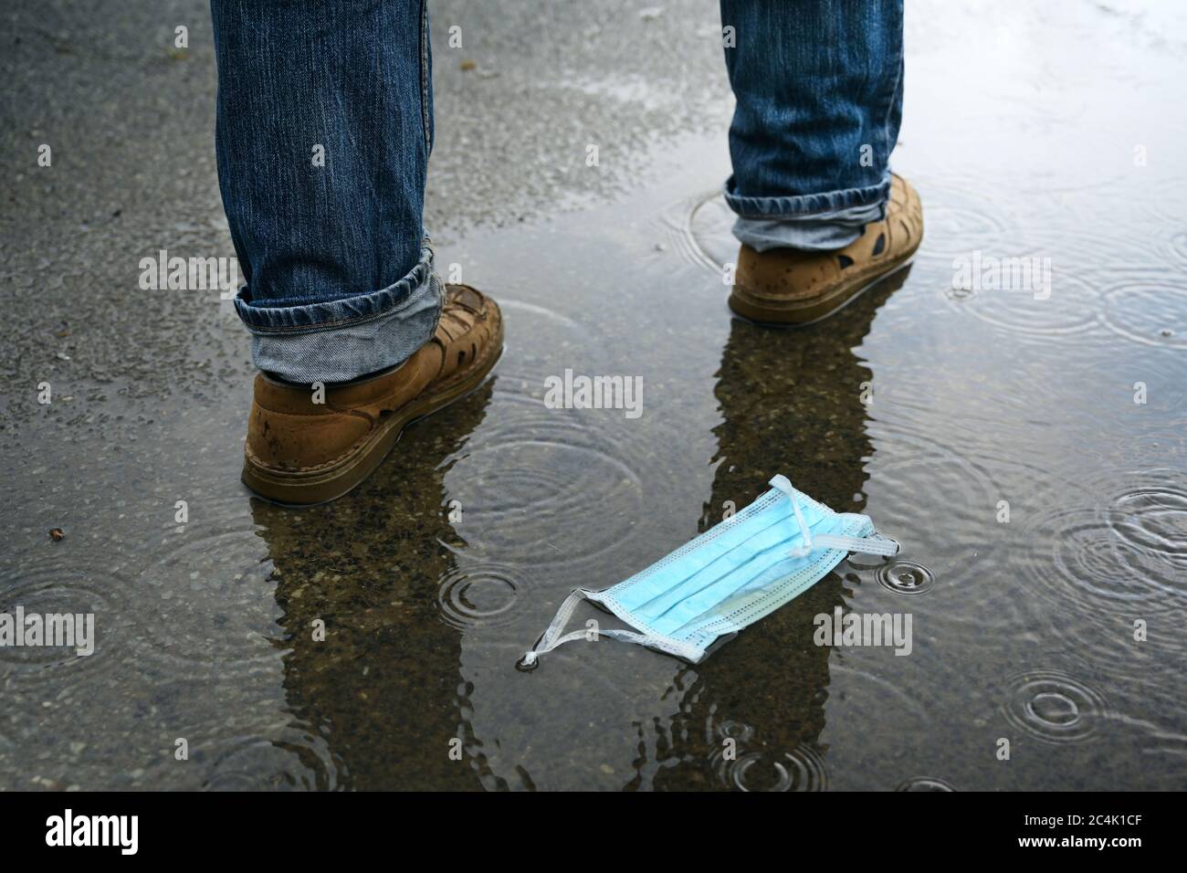 Man passes by after throwing away his face mask on the rainy street, but the danger of coronavirus infection could still exist also after the end of l Stock Photo