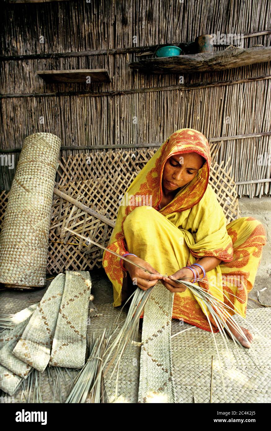 A woman works with the stems of some palm or coconut leaves used