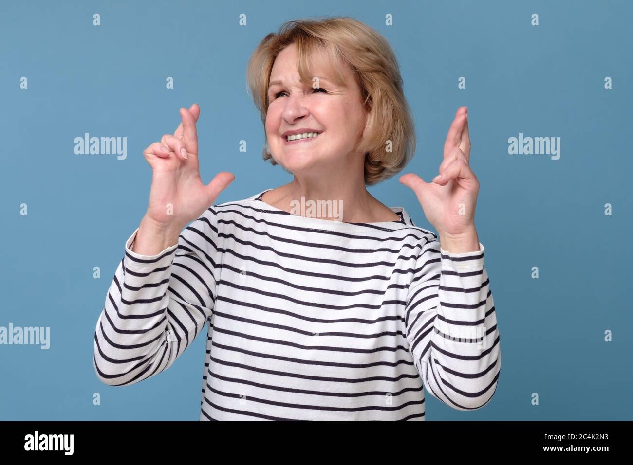 Mature caucasian woman holding fingers crossed wishing a luck Stock Photo