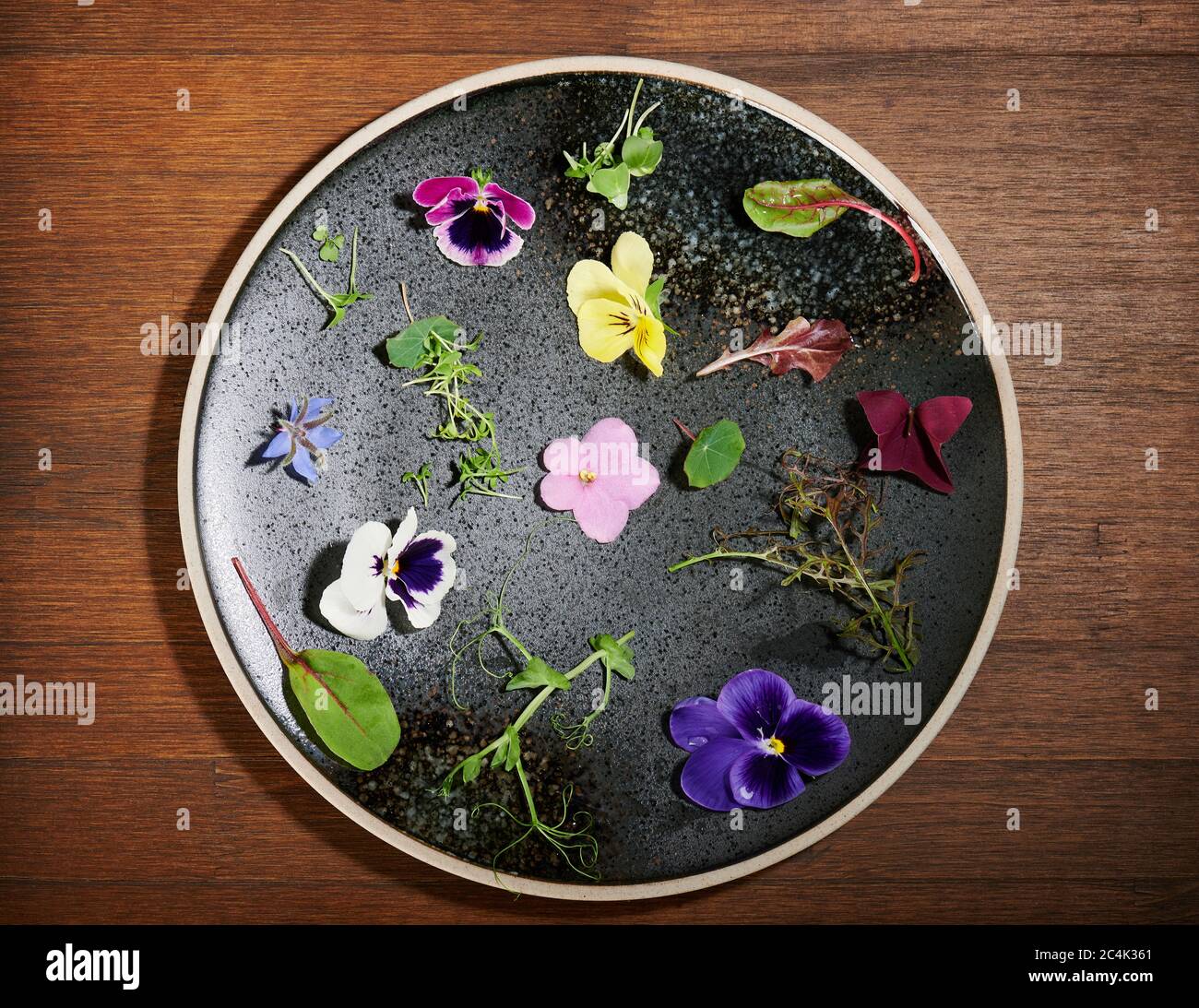 Eatable flower dressing assortment on black plate above top view Stock Photo