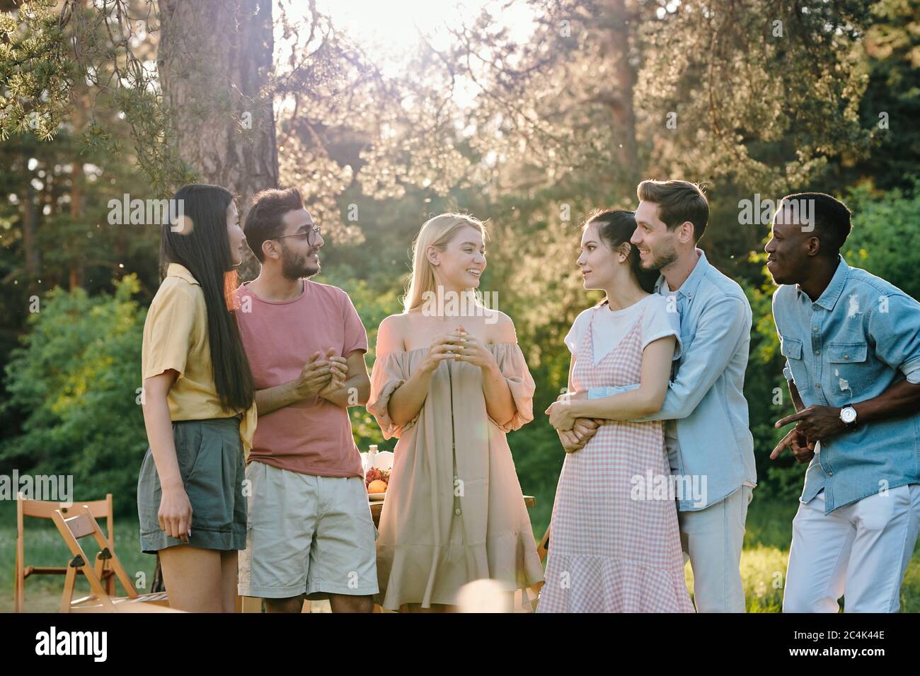 Company of three happy young couples in casualwear discussing news or their plans for summer while gathered together in park Stock Photo