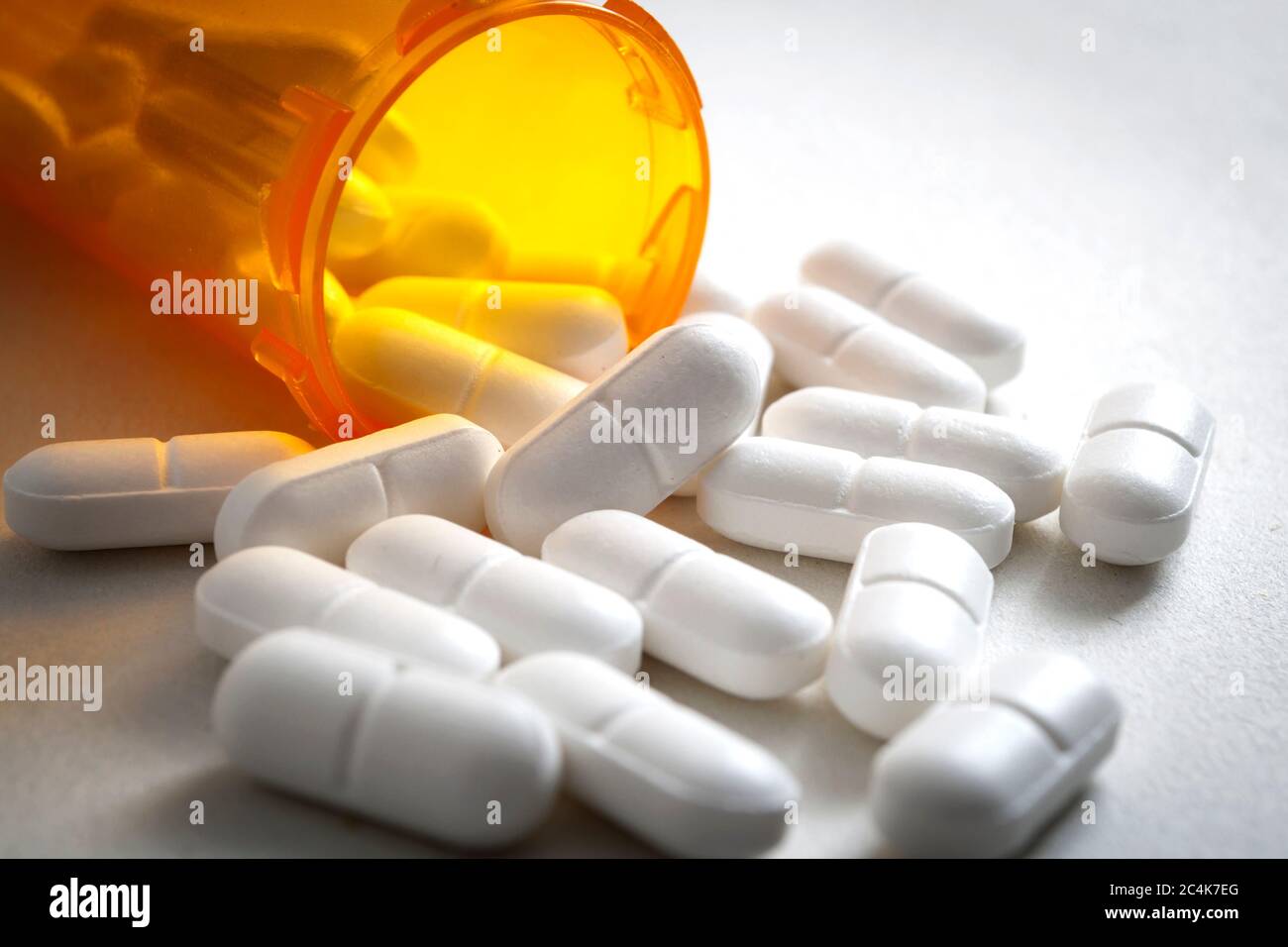 Opioid epidemic, painkillers and drug abuse concept with close up on a bottle of prescription drugs and hydrocodone pills falling out of it on white Stock Photo