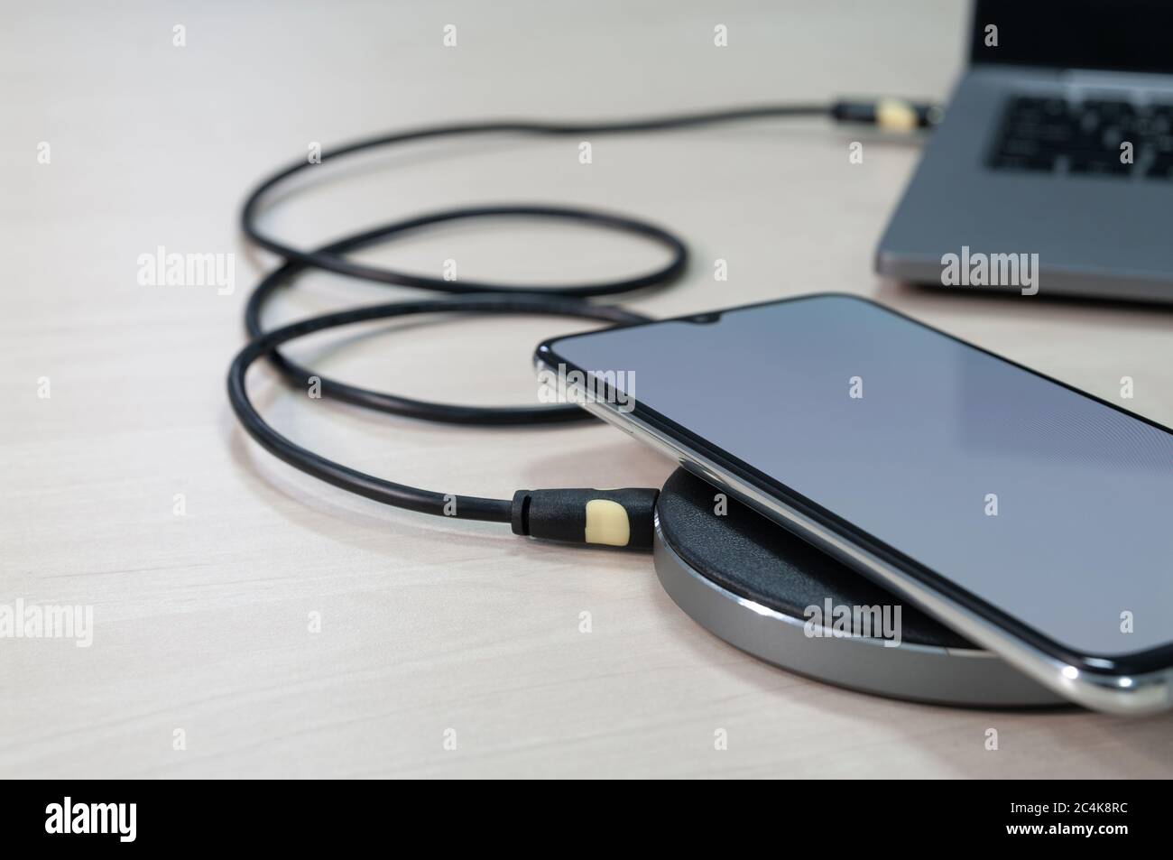 Modern smartphone are charging from wireless charger lies next to the laptop on a wooden table. Modern technology concept. Selective focus Stock Photo