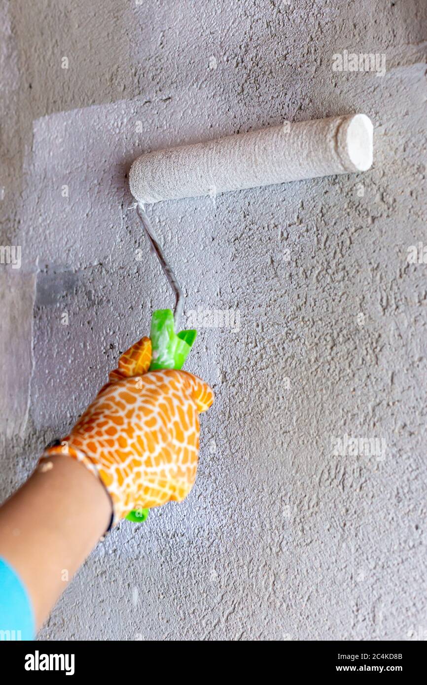 Cement wall painting with white paint and roller. Yellow gloves Stock