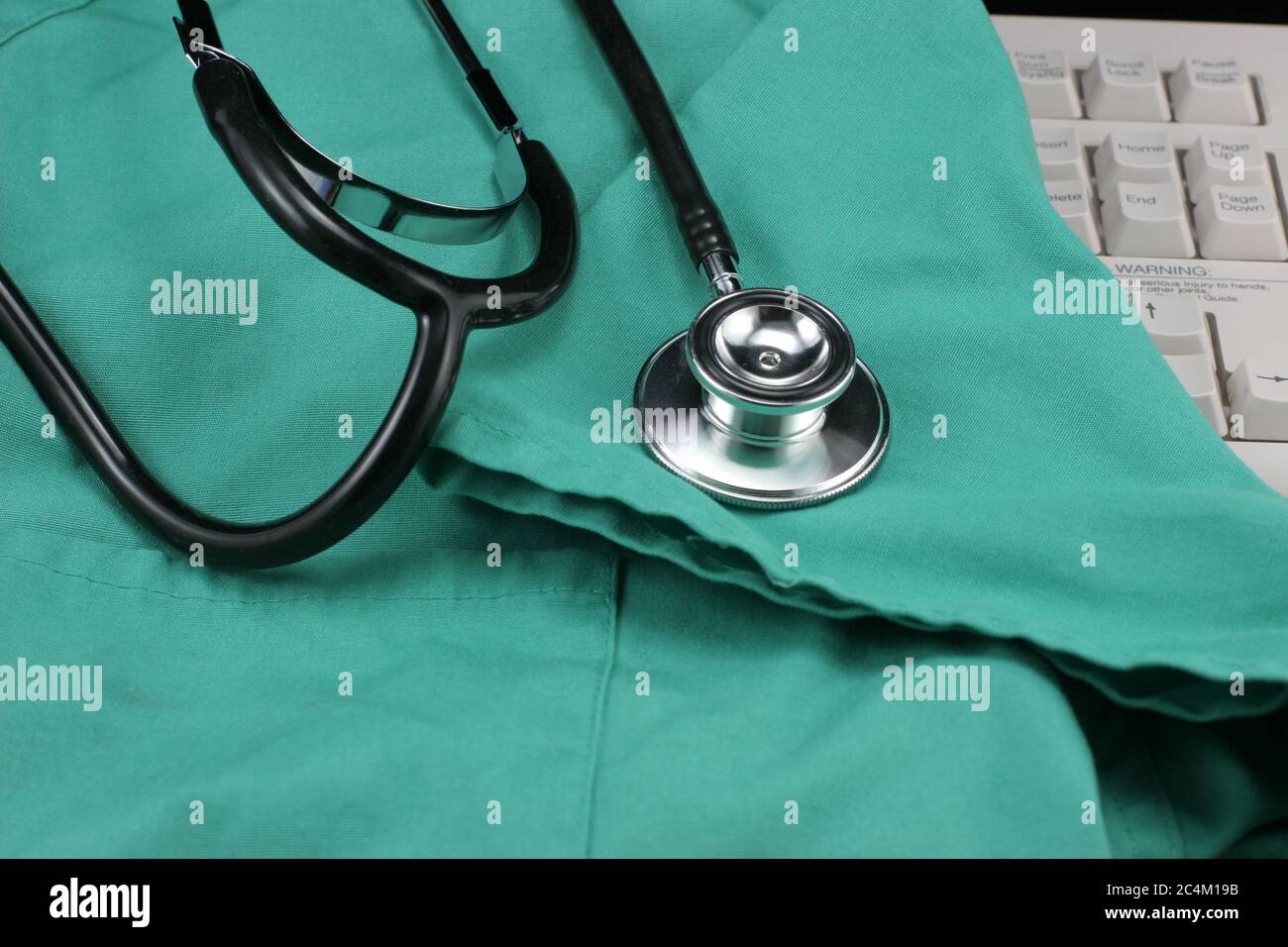 Medical stethoscope.on top of green scrubs & computer keyboard for entry of patient medical records. Stock Photo