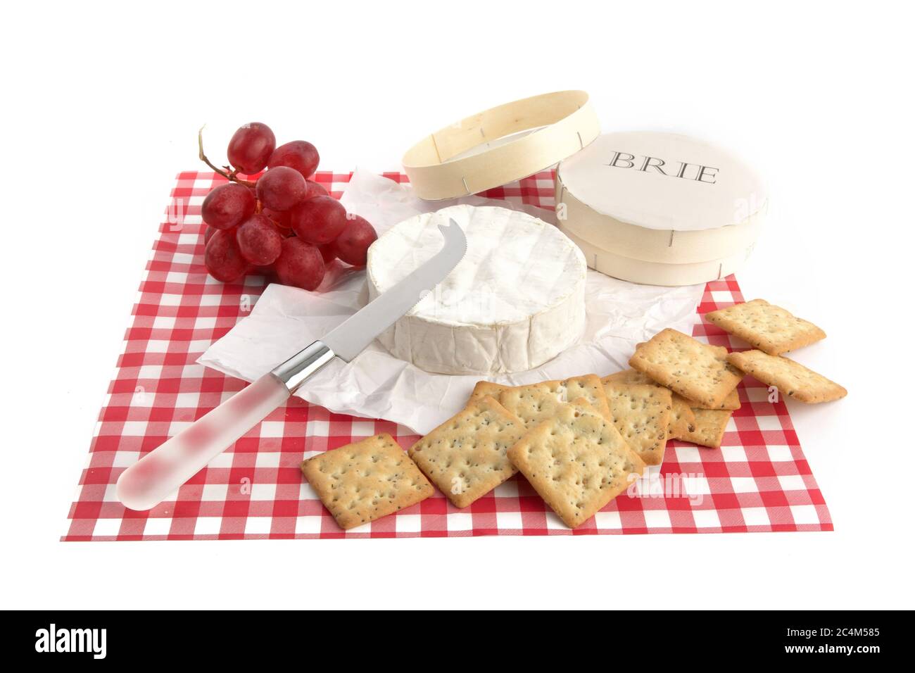 a round of brie cheese with crackers and grapes on a red checked place