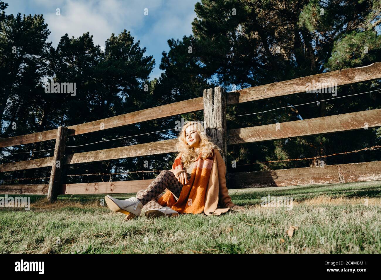 A young asian woman sitting near a wooden fence in nature. Stock Photo