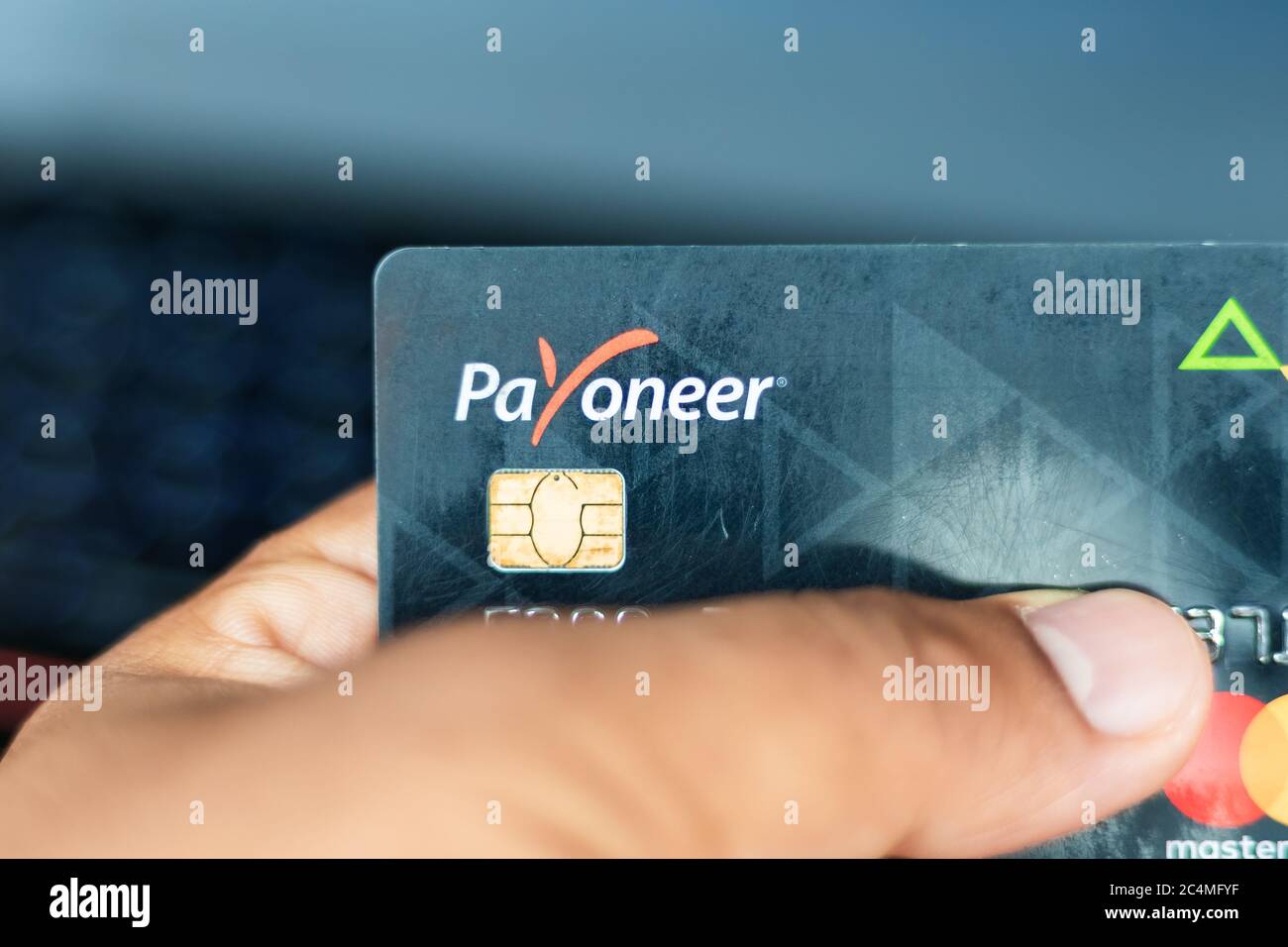 Bhairahawa, Nepal - June 27 2020: Man holds Payoneer Prepaid MasterCard against laptop computer. Payoneer funds were recently put on hold due to insol Stock Photo