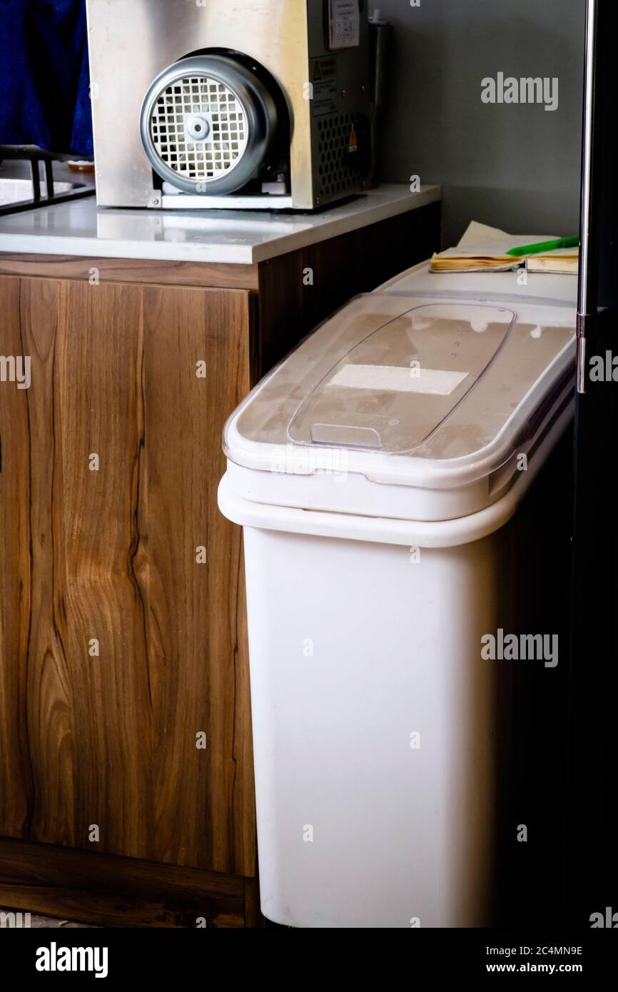 A white plastic garbage bin with clear cover standing beside wooden