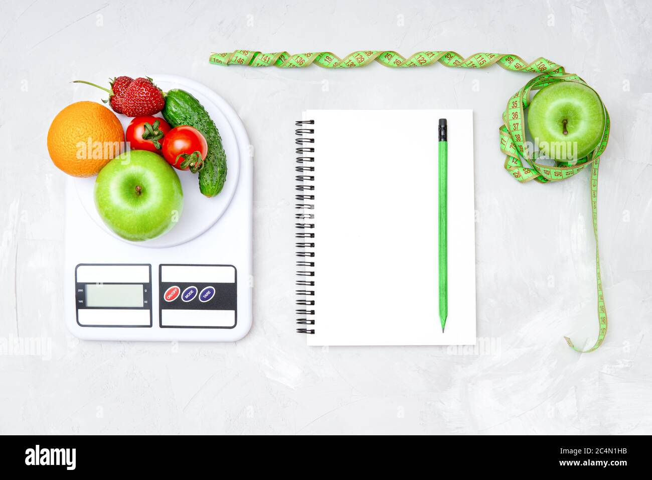 Healthy weight loss meal plan. Flat lay of a whole apple wrapped with measuring tape, kitchen scales with vegetables and fruits, blank paper notebook Stock Photo