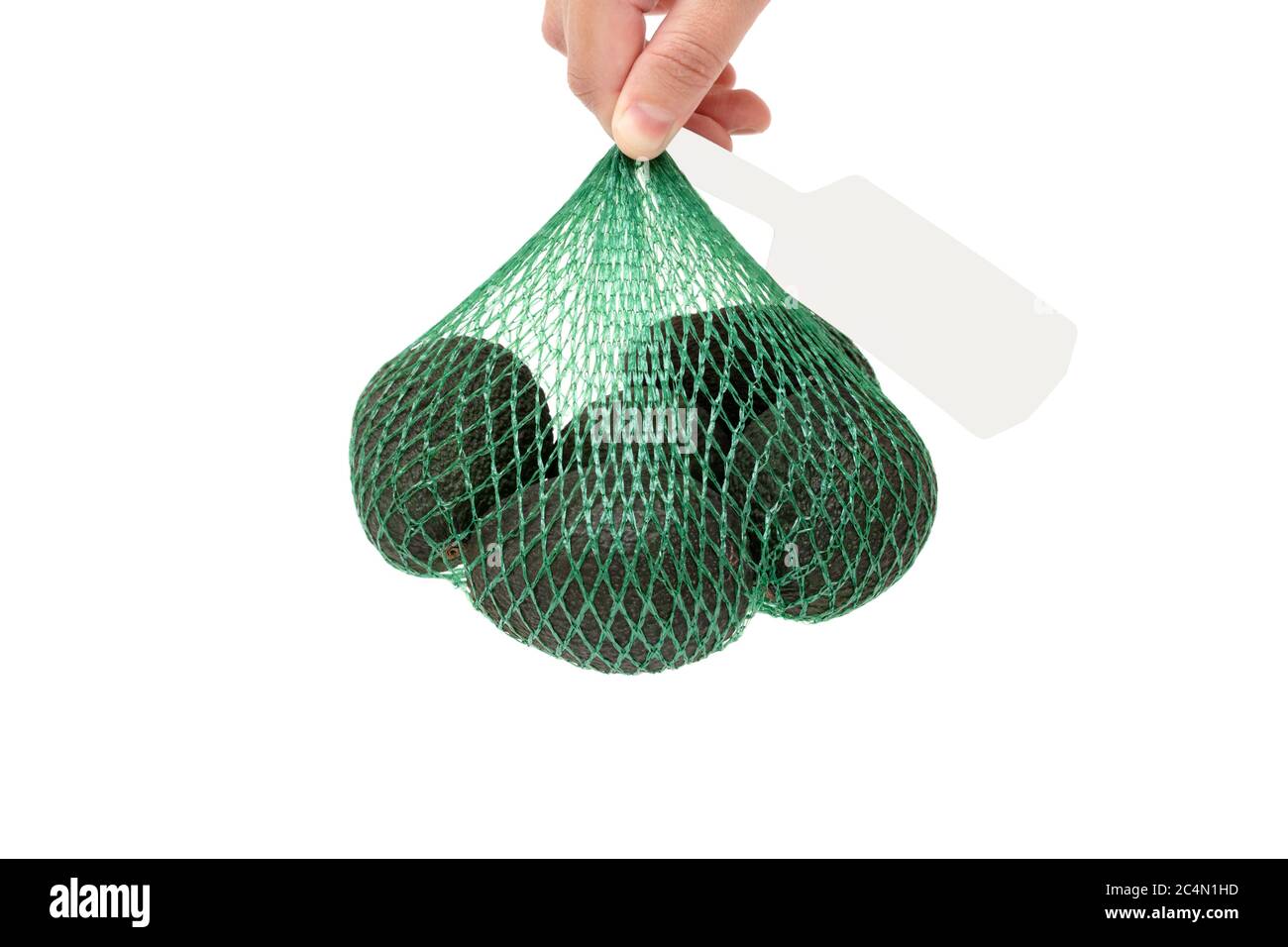Female hand holding a fresh organic hass avocados in a green mesh bag with a grey tag isolated on white. Healthy food concept. Stock Photo