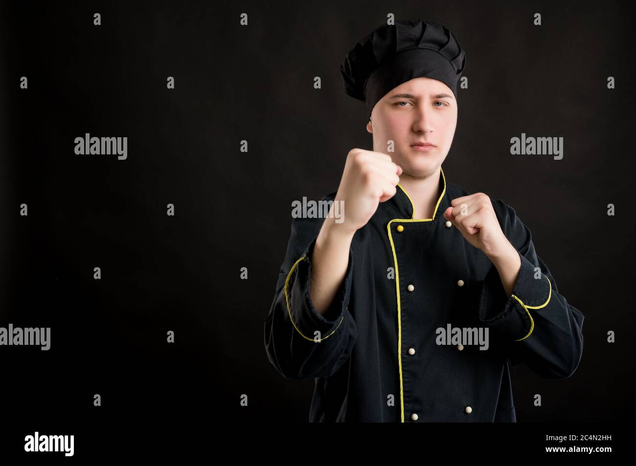 Portrait of young male dressed in a black chef suit showing fists ...