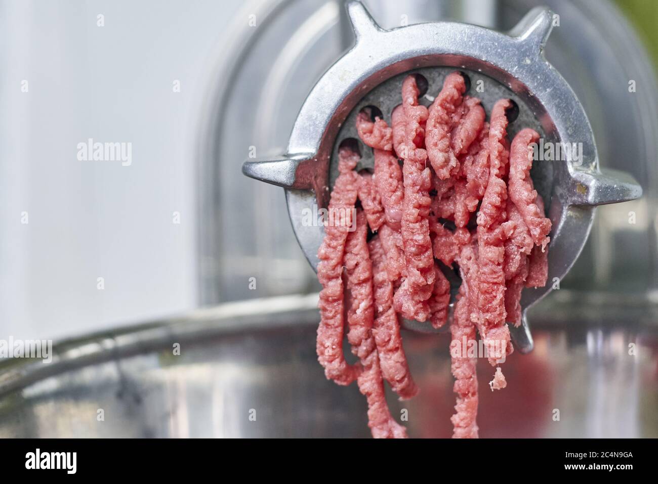 Meat grinder in action and ground beef meat. electric meat grinder.  Unidentifiable butcher holding tray full of minced raw red meat leaving  machine in Stock Photo - Alamy