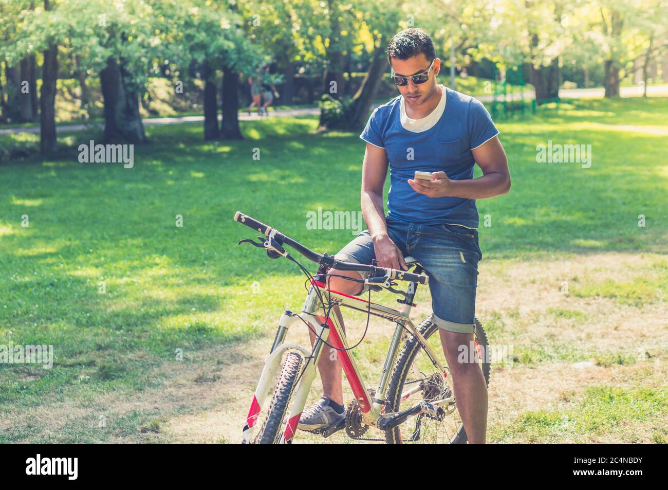 Young Indian man on bicycle watching his smartphone in the park Stock Photo