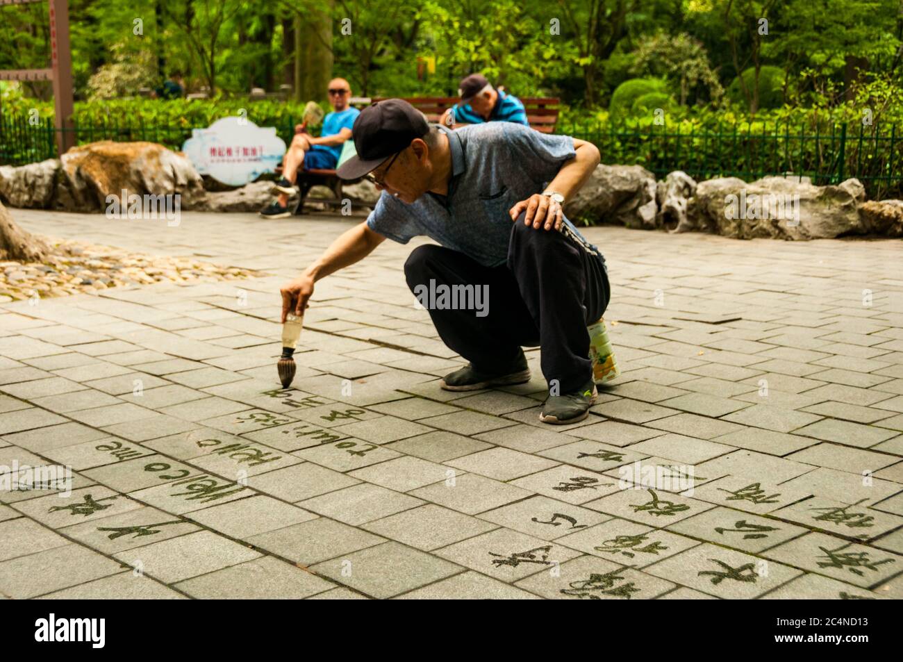 An old man writes calligraphy using a water brush in Shanghai’s Lu Xun Park. Stock Photo