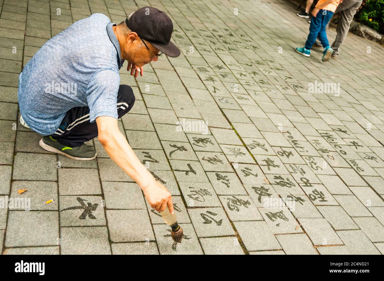 An old man writes calligraphy using a water brush in Shanghai’s Lu Xun Park. Stock Photo