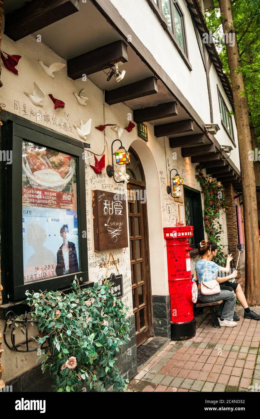 A young couple take a picture using a selfie stick in front of Tianai (sweet love) Lounge on Hongkou’s Tianai Road in Shanghai. Stock Photo