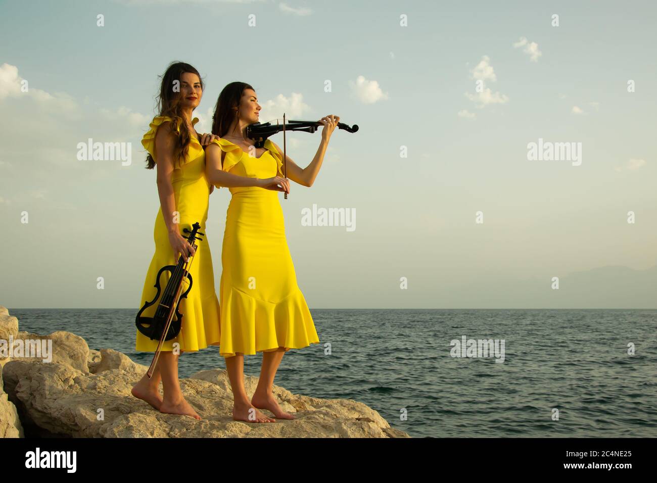 Two beautiful girls violinists in yellow concert dresses are playing electric violins with
