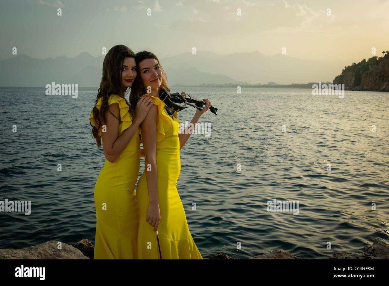 Two beautiful girls violinists in yellow concert dresses are playing electric violins with