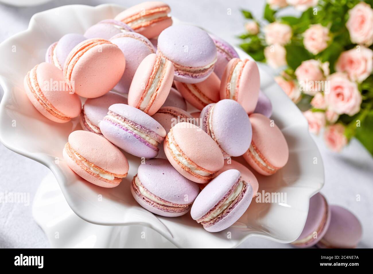 french macarons on a porcelain cake stand with beautiful bouquet of roses and creamer at the background, horizontal view, close-up, macro Stock Photo
