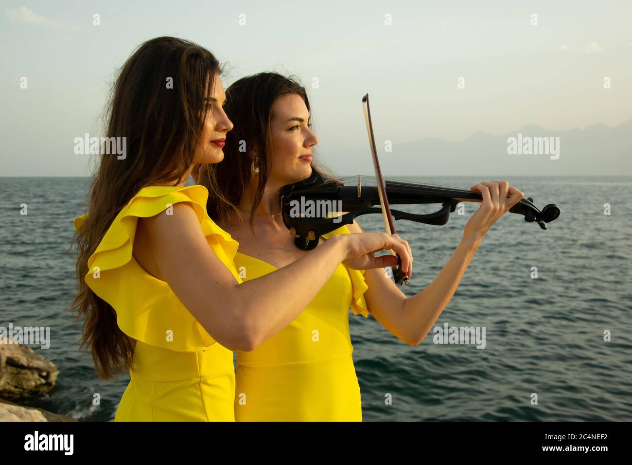 Two beautiful girls violinists in yellow concert dresses are playing electric violins with