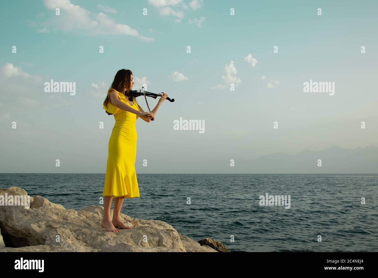 Beautiful violinist girl in yellow concert dress is playing electric