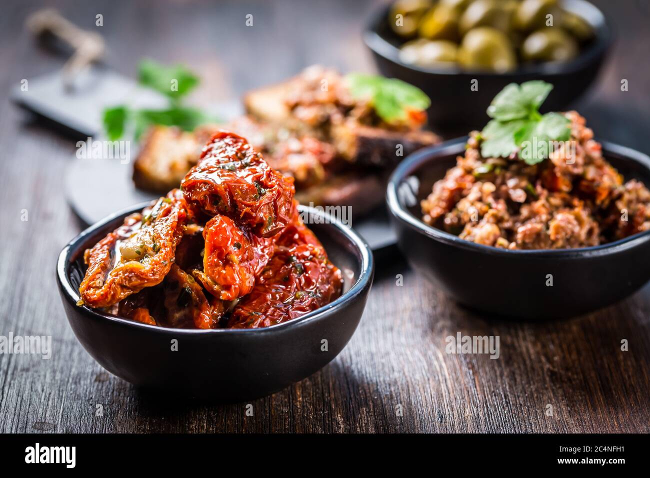 Sun dried tomato with olive oil as antipasto with tapenade and bruschetta in background Stock Photo