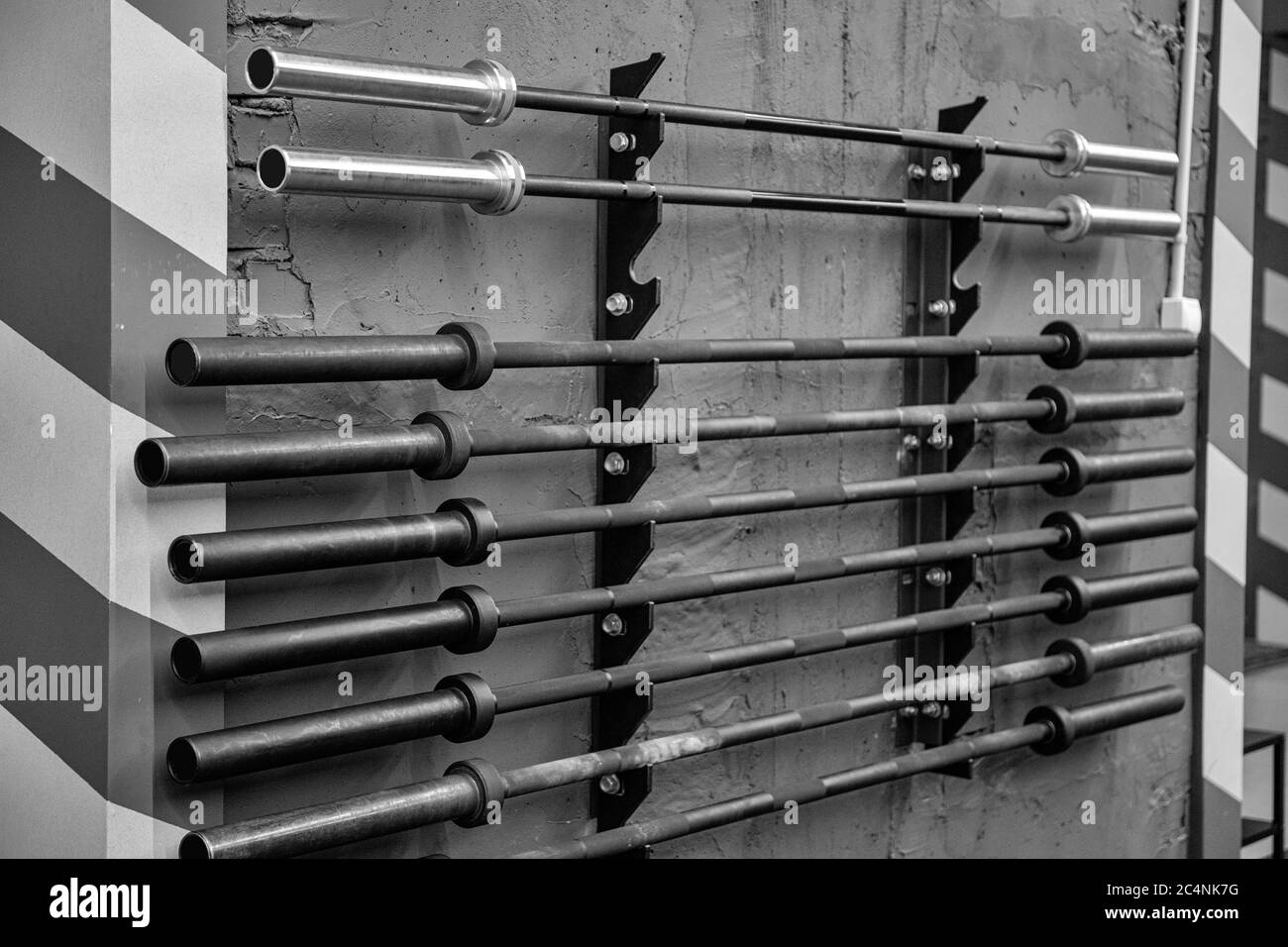 Fitness equipment for workout in Gym. Barbell without weights on row. Disassembled barbells on wall in fitness center. Stock Photo