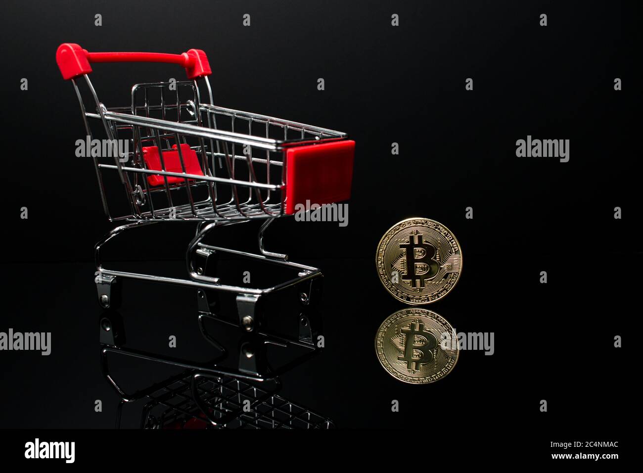 A shopping cart with a crypto currency Bitcoin coin next to it with a black background. Stock Photo