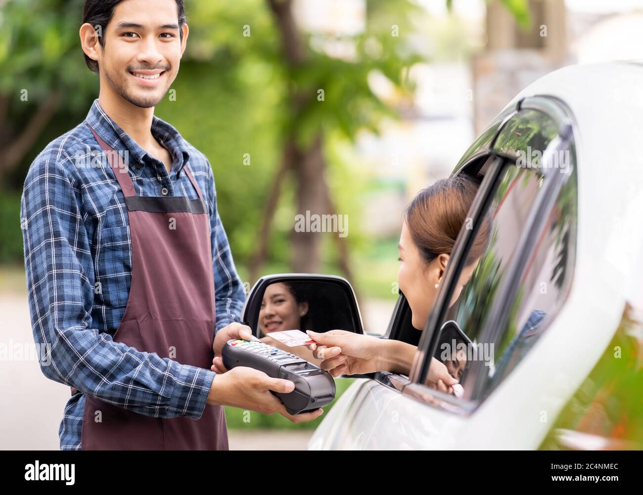 Portrait of asian restaurant employer hold credit card reader for asian woman customer to make mobile payment contactless technology on drive thru foo Stock Photo
