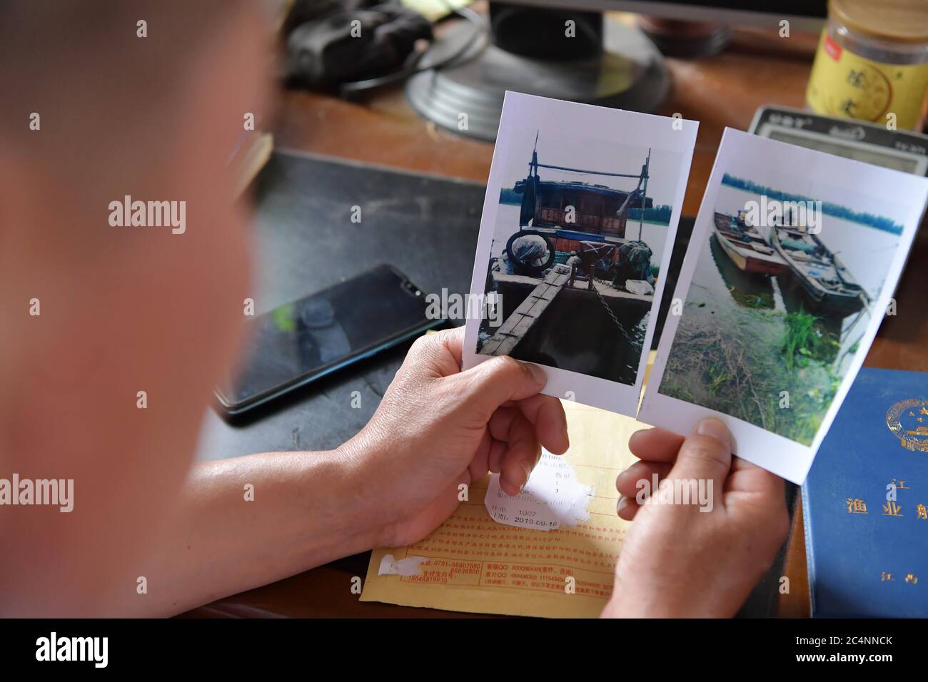 (200628) -- NANCHANG, June 28, 2020 (Xinhua) -- Wu Huashan displays photos of the fishing boats he once owned in Xiangshan Township, Nanchang, east China's Jiangxi Province, June 5, 2020. Having learned fishing at an early age with his parents, Wu was a skilled fisherman and was head of a local fishery association. In late 2019, he bade farewell to his boats and started a crayfish business. China began a 10-year fishing moratorium from the beginning of this year in 332 conservation areas in the Yangtze River basin, which will be expanded to all the natural waterways of the country's longest r Stock Photo