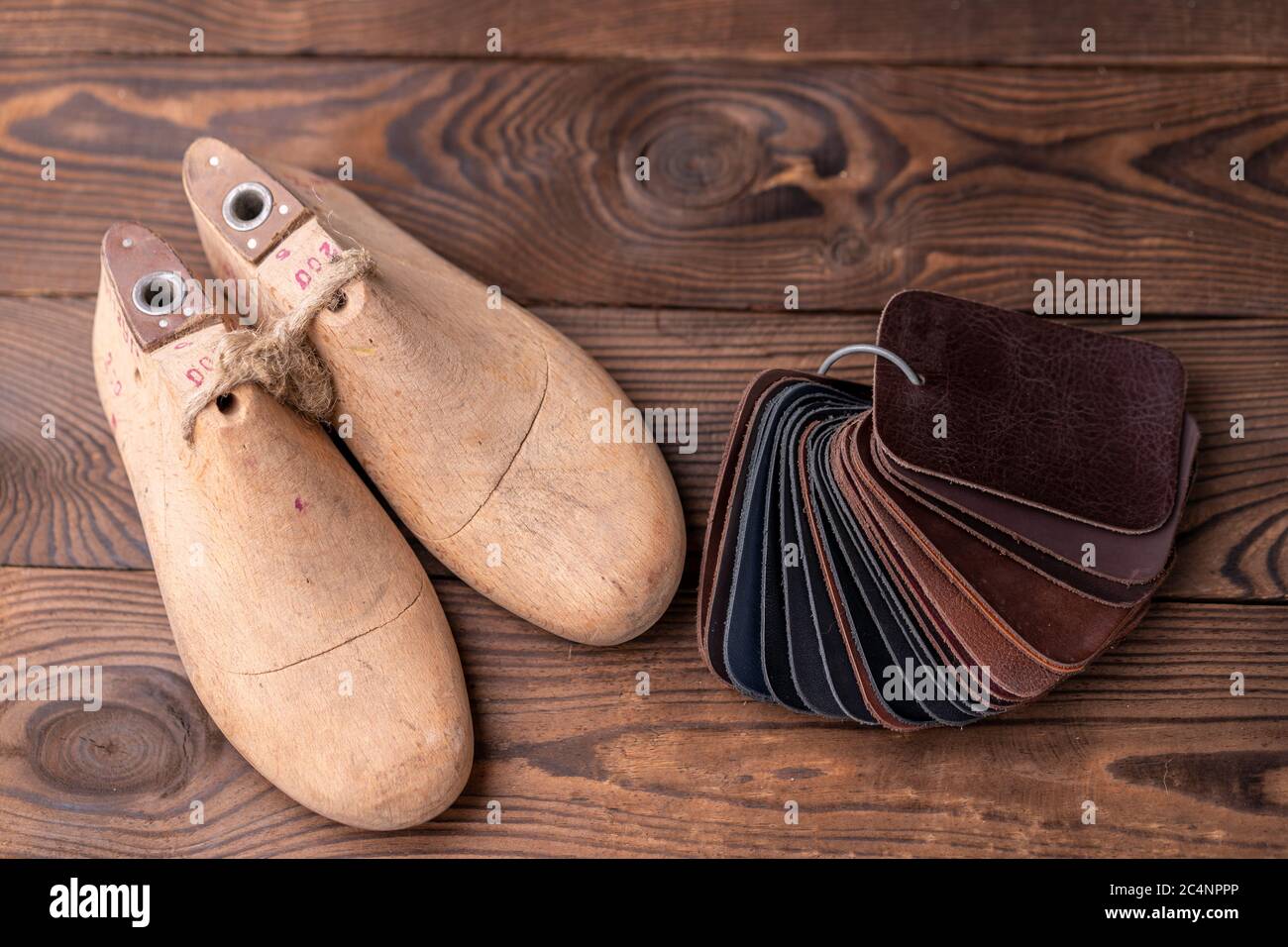 Leather samples for shoes and wooden shoe last on dark wooden table. Designer furniture clothes. Shoe maker workspace. Stock Photo