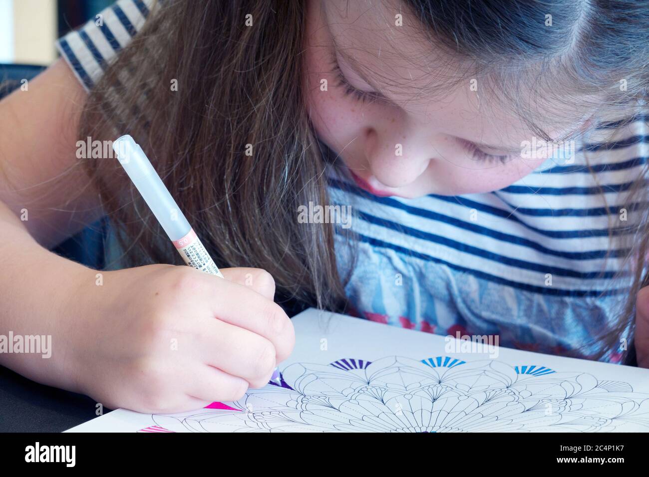 A child sat at home and concentrating hard colouring in an adult colouring book with assorted coloured pens Stock Photo