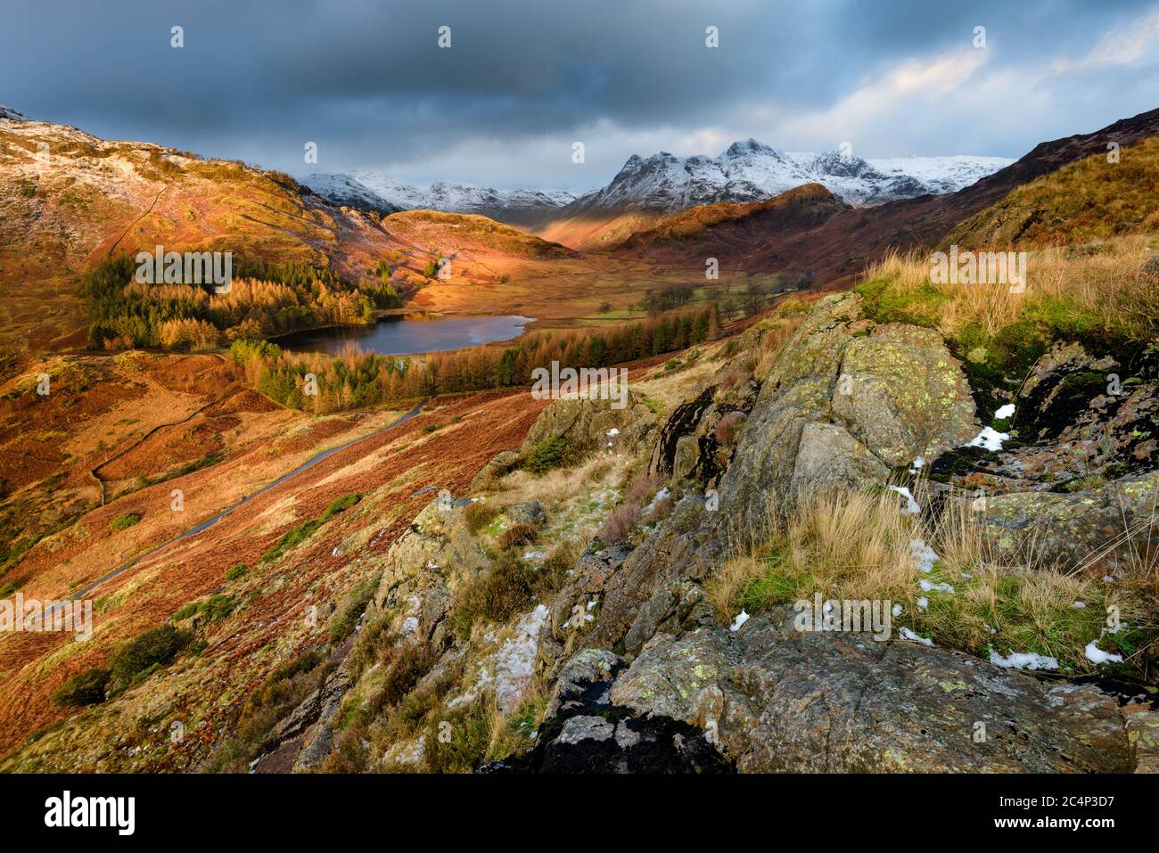 Ultra Wide View Of Dramatic Landscape Blea Tarn With Snow On Langdale Pikes And Dark Moody Clouds. Lake District, UK. Stock Photo