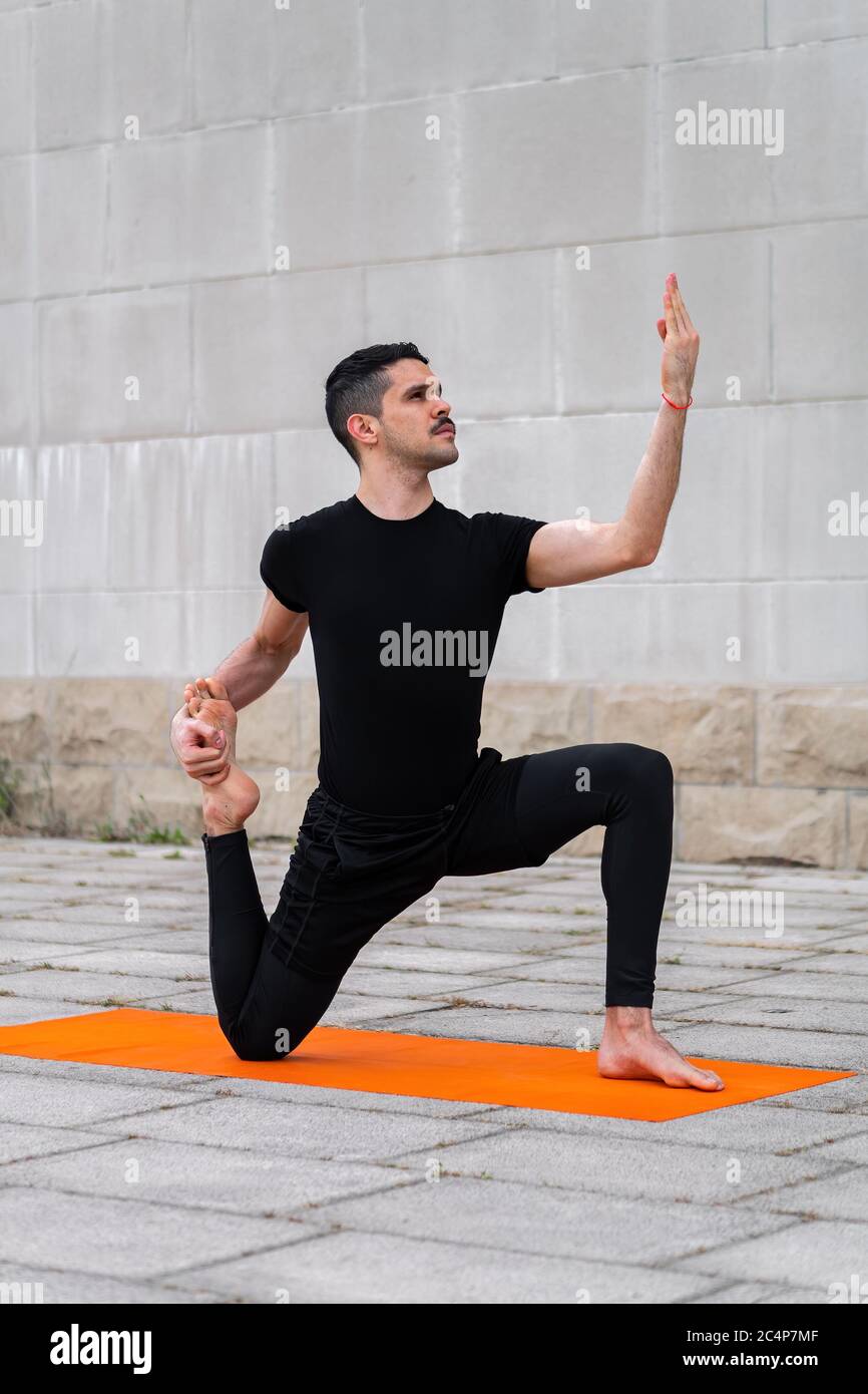 Handsome sporty latin man exercising in a city, doing yoga, sitting in variation of One Legged King Pigeon Pose. Stock Photo