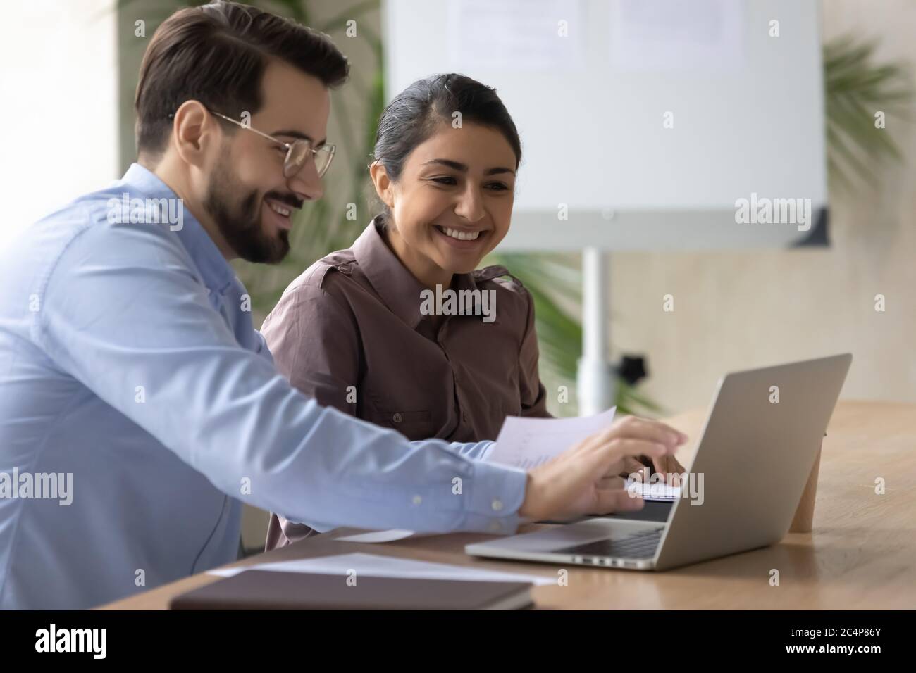 Smiling diverse colleagues working on project together, using laptop Stock Photo
