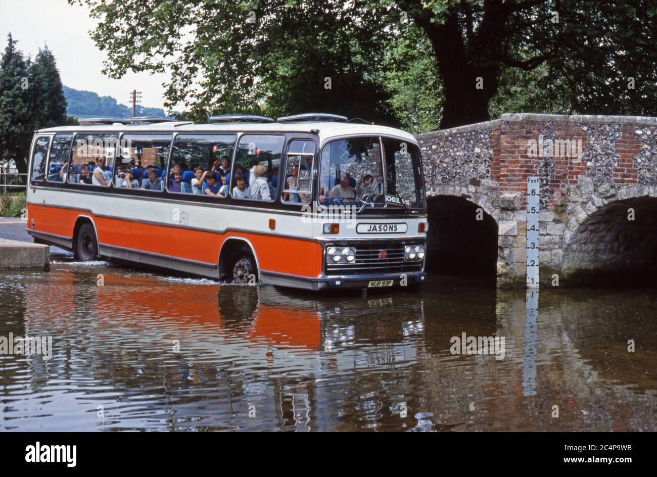 Coach, acting as school bus, passing through the water of the ford at Eynsford, Kent, England, much to the excitement of the children on board Stock Photo