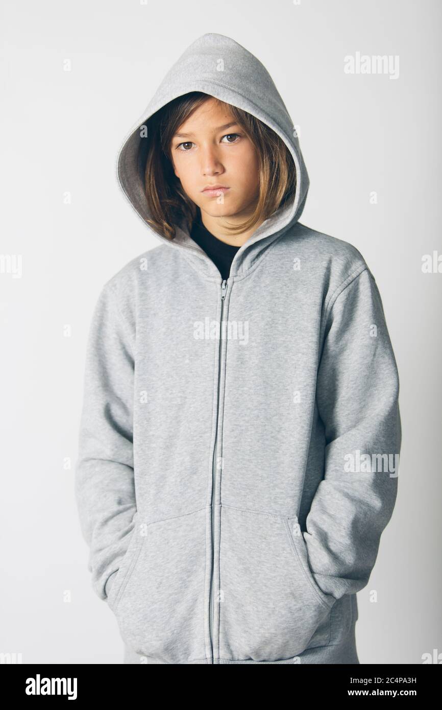Eleven years old boy with hooded sweater standing against a white background Stock Photo