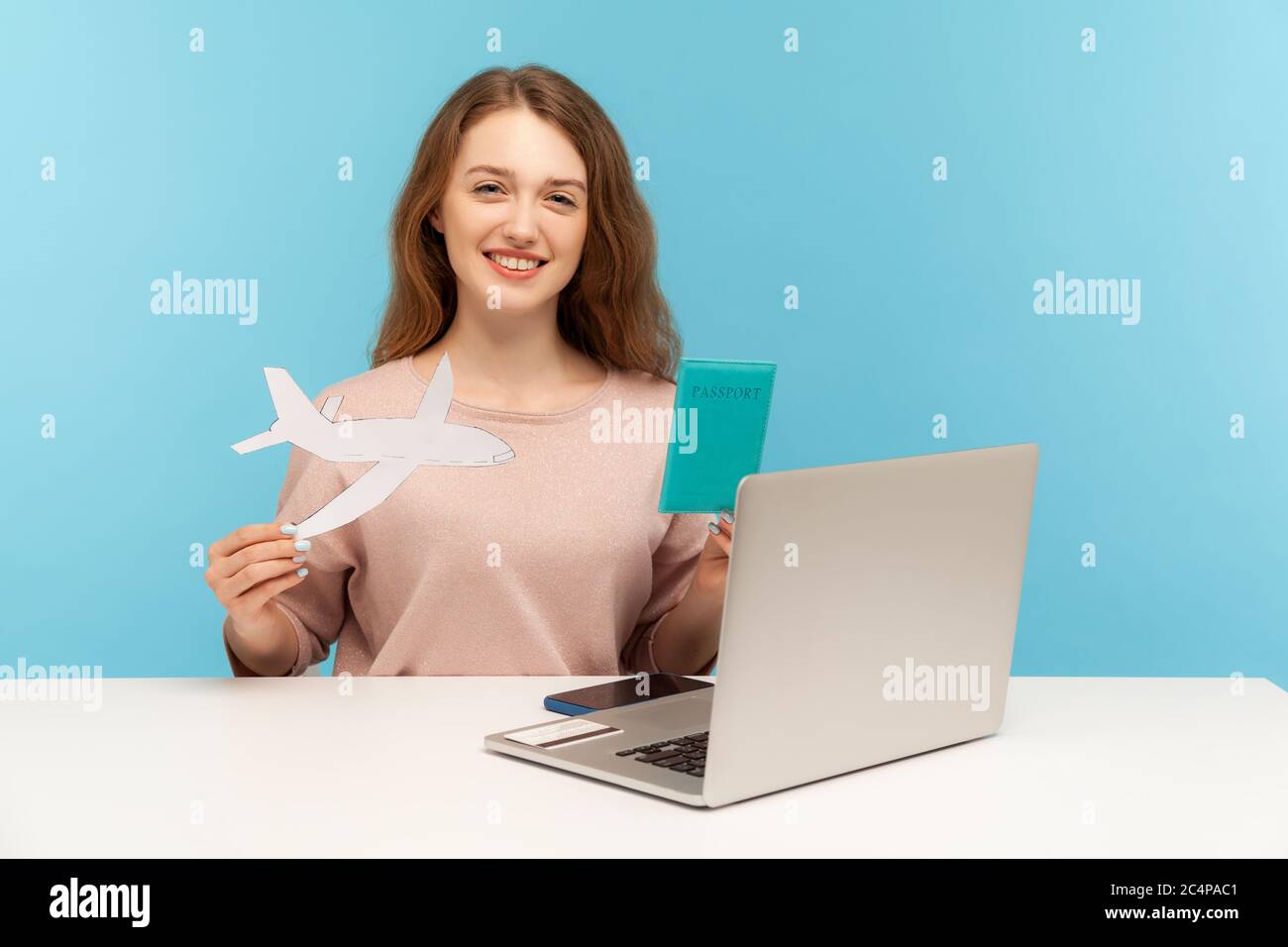 Friendly woman, travel agent holding passport and paper airplane, looking at camera with toothy smile, advertising hot tours with airline transportati Stock Photo